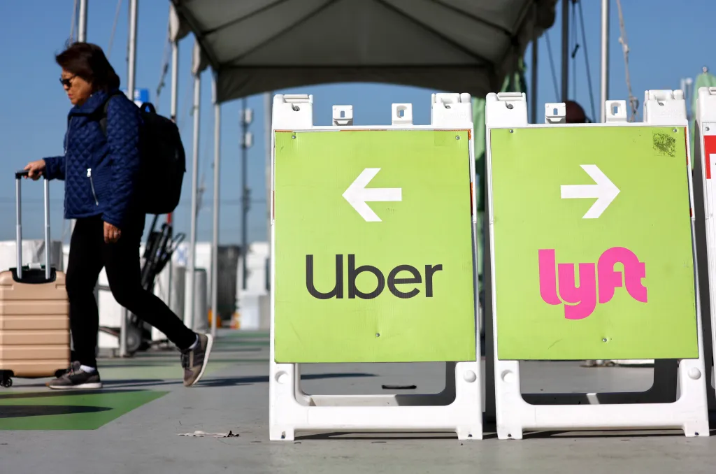 A person with luggage walks past signs directing to Uber and Lyft pickup areas at Los Angeles International Airport.