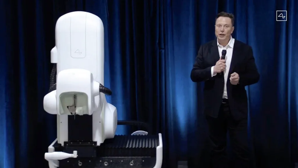 Elon Musk stands next to a surgical robot during a Neuralink presentation.