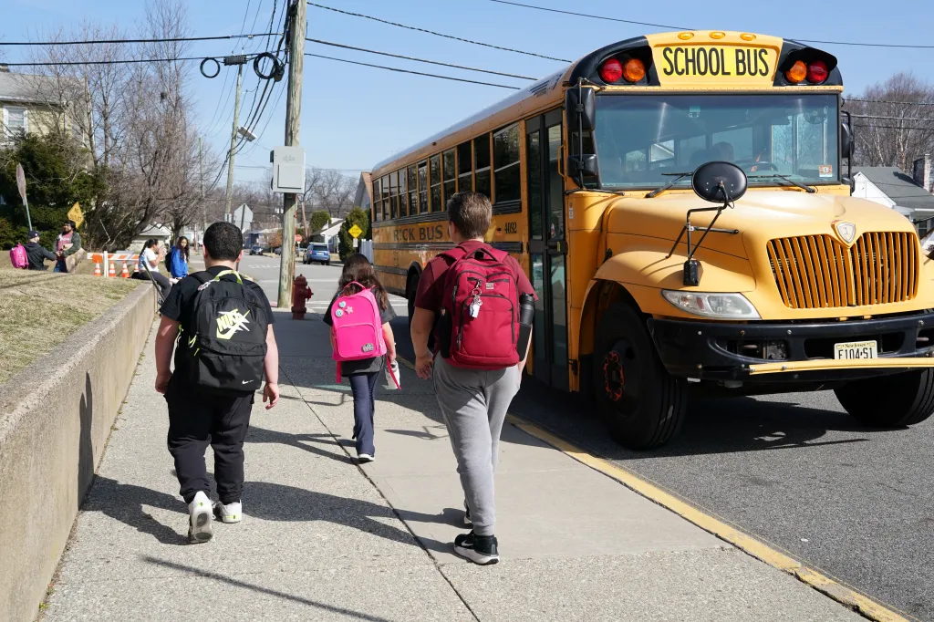 Students with backpacks walking past a yellow school bus.
