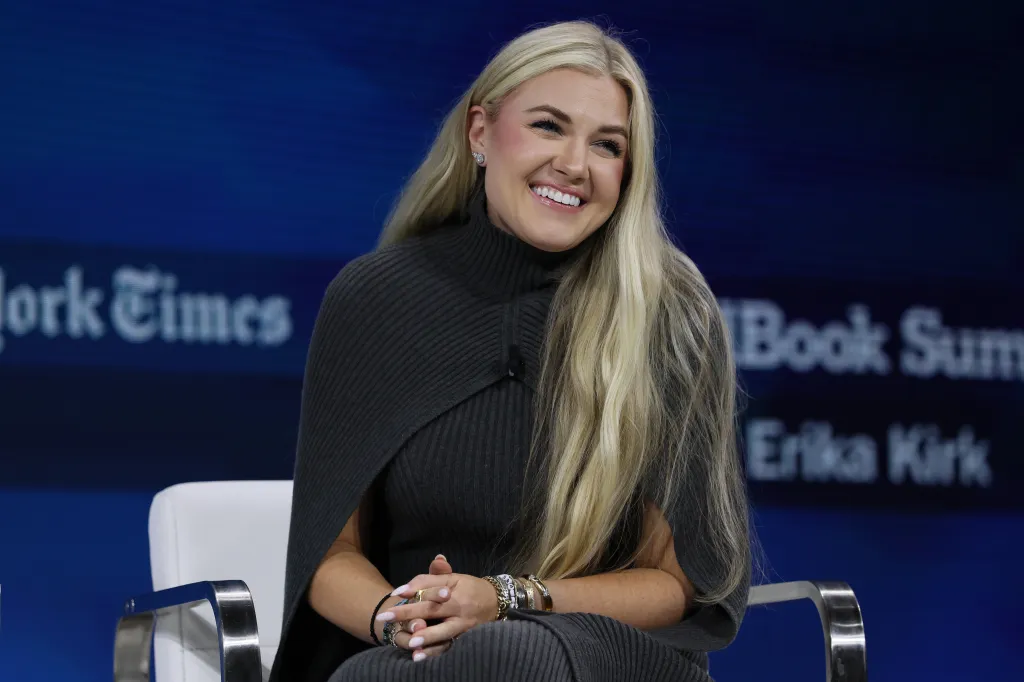 Erika Kirk, with long blonde hair, smiles while seated at the 2025 New York Times Dealbook Summit.