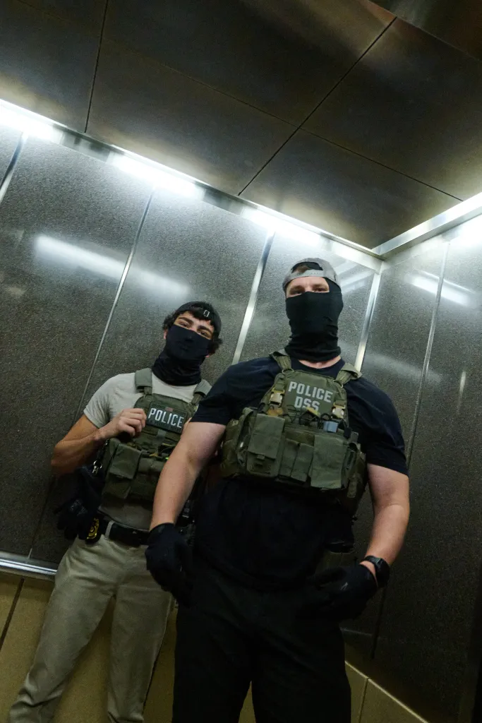 Two masked federal agents from ICE, wearing tactical vests, are seen in an elevator.