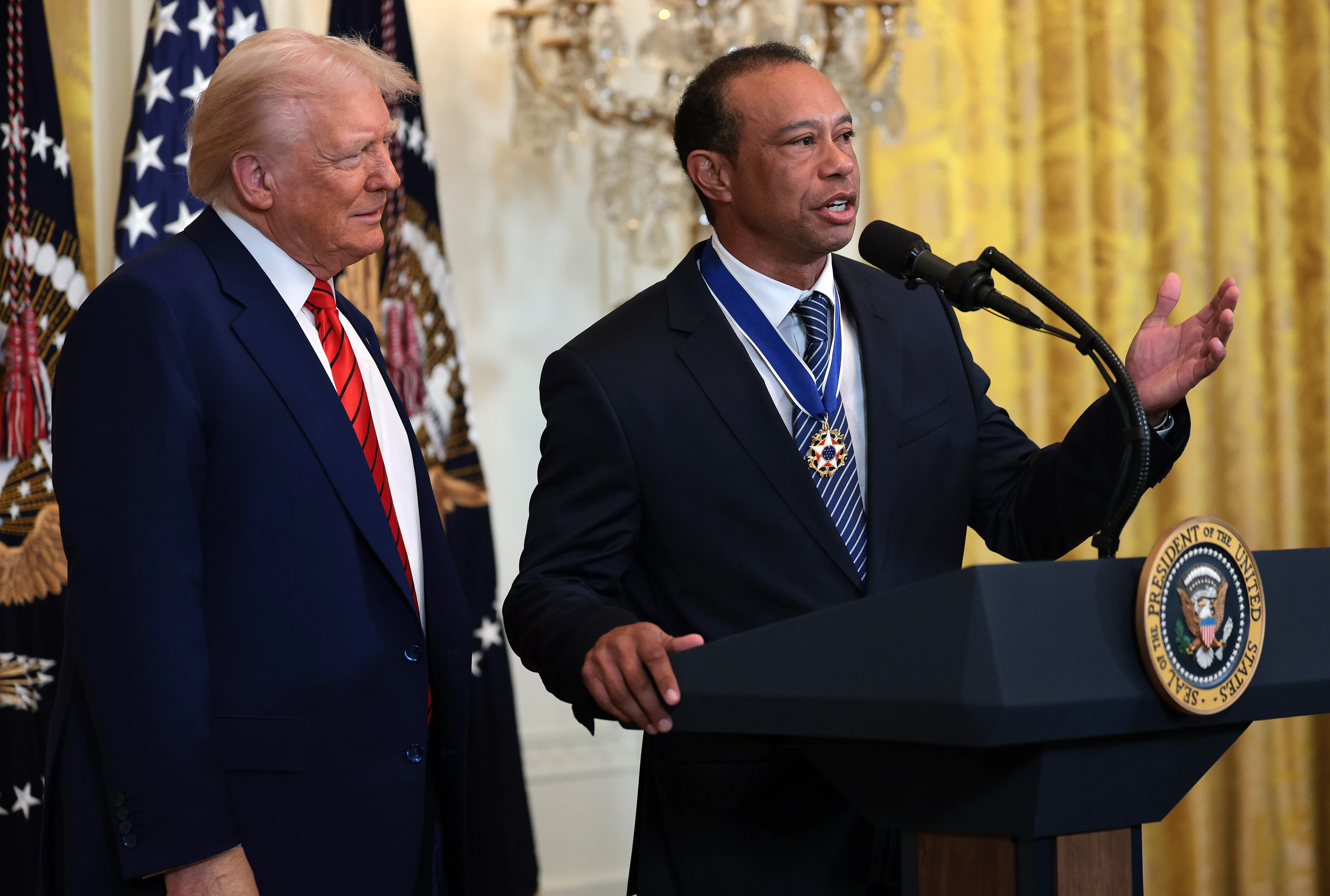Tiger Woods speaking at a podium next to President Donald Trump during a Black History Month reception at the White House.
