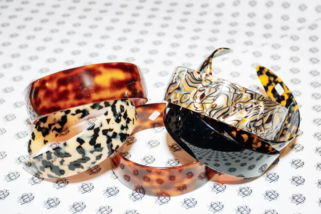 Four hair clips with various tortoiseshell patterns, placed on a white surface with a patterned print.