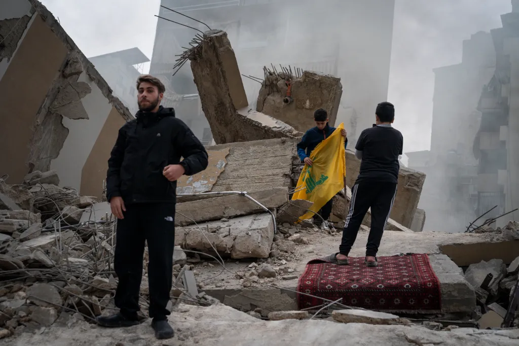 Men stand among the debris of a building in Beirut, Lebanon, with one holding a Hezbollah flag.