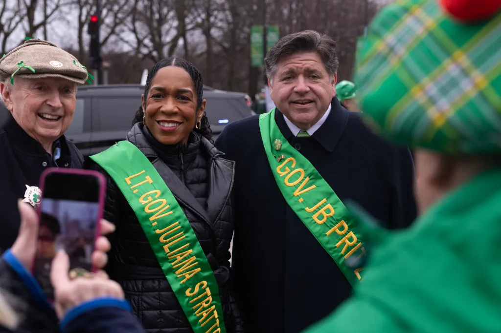 Lt. Governor Juliana Stratton and Governor JB Pritzker smiling while wearing green sashes.