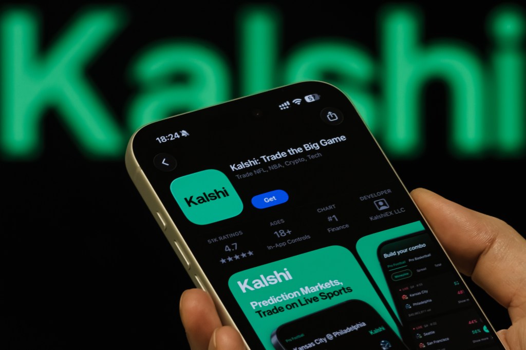 Photo illustration of a hand holding a smartphone displaying the Kalshi app page on the Apple App Store, with 