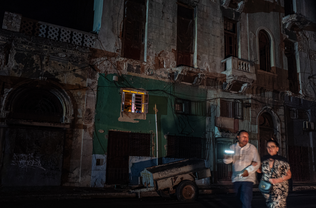 Two people walk on a dark street, lit by a flashlight, during a nationwide blackout in Havana.