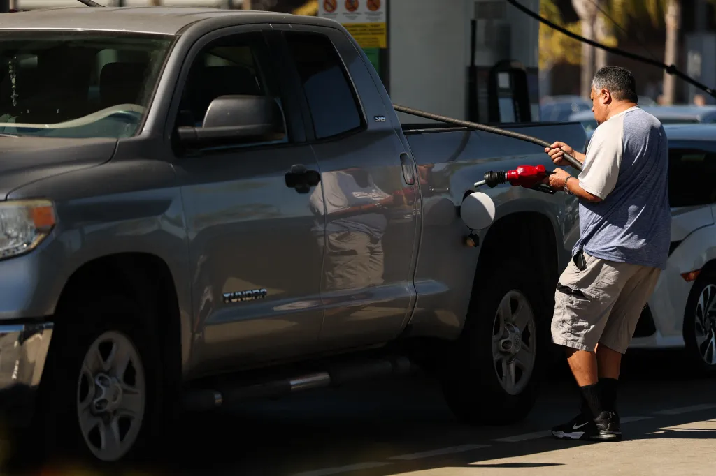 A man refueling a grey pickup truck at a gas station.