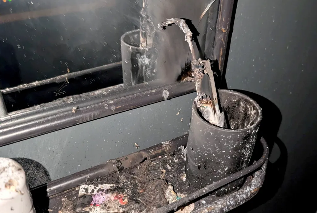 Melted and charred debris from an exploded electric toothbrush on a bathroom shelf.