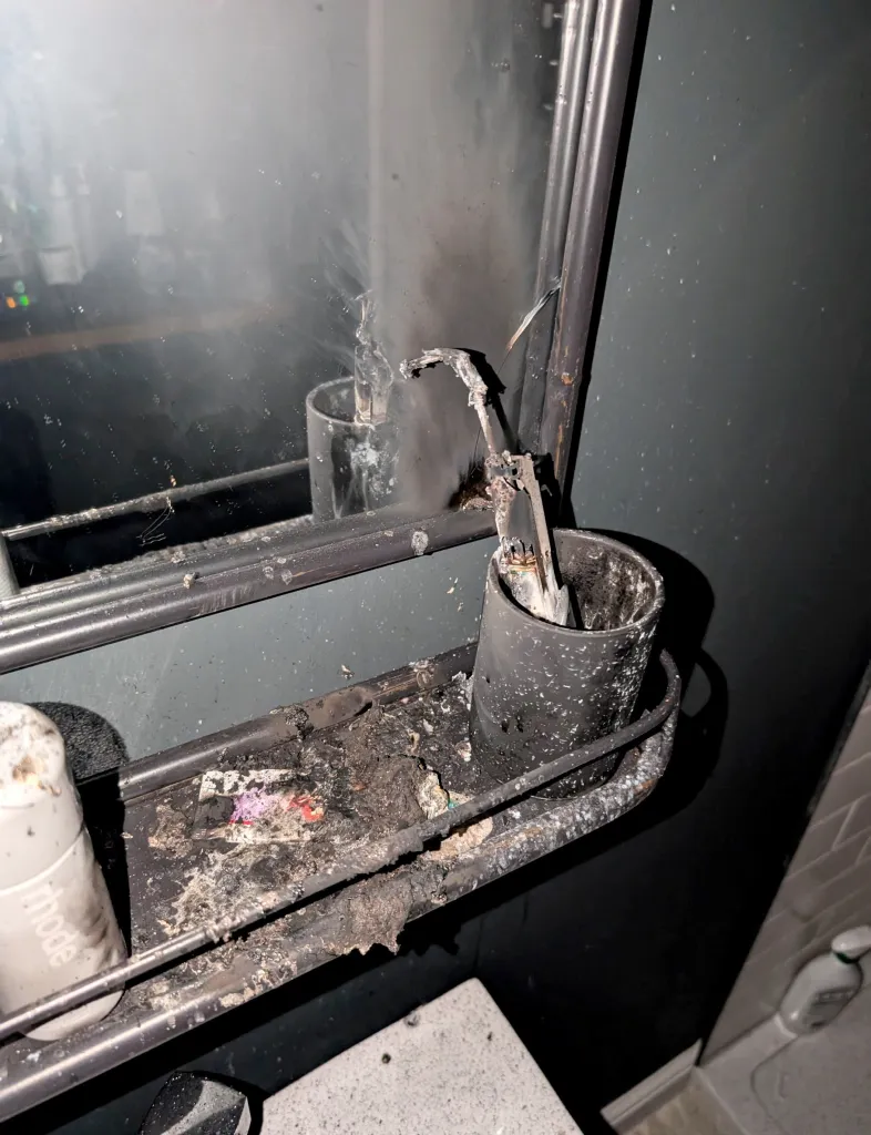 Melted electric toothbrush and debris in a metal holder in a smoke-damaged bathroom.