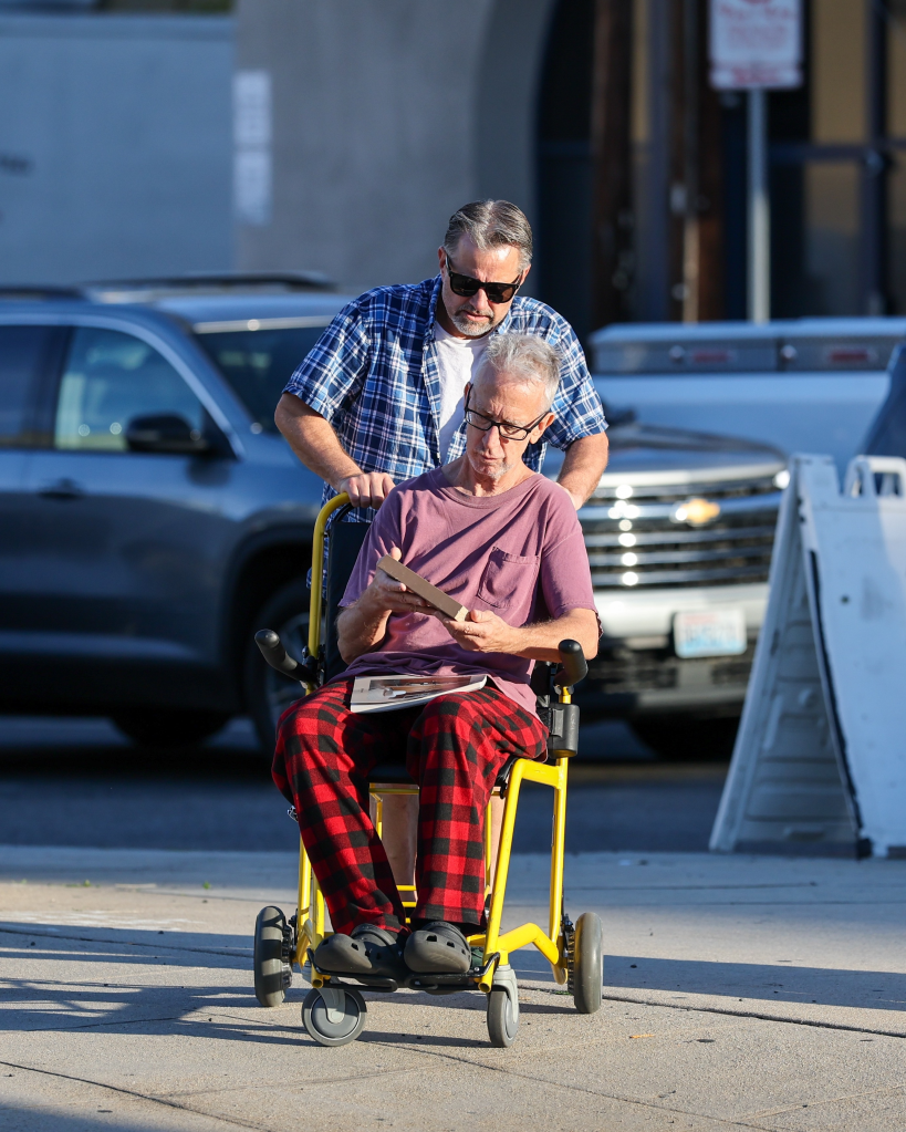 Andy Dick in a wheelchair being pushed by a companion during an outing.