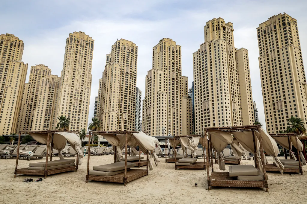 Empty beach beds and lounge chairs on Jumeirah Beach in Dubai, with tall buildings in the background.