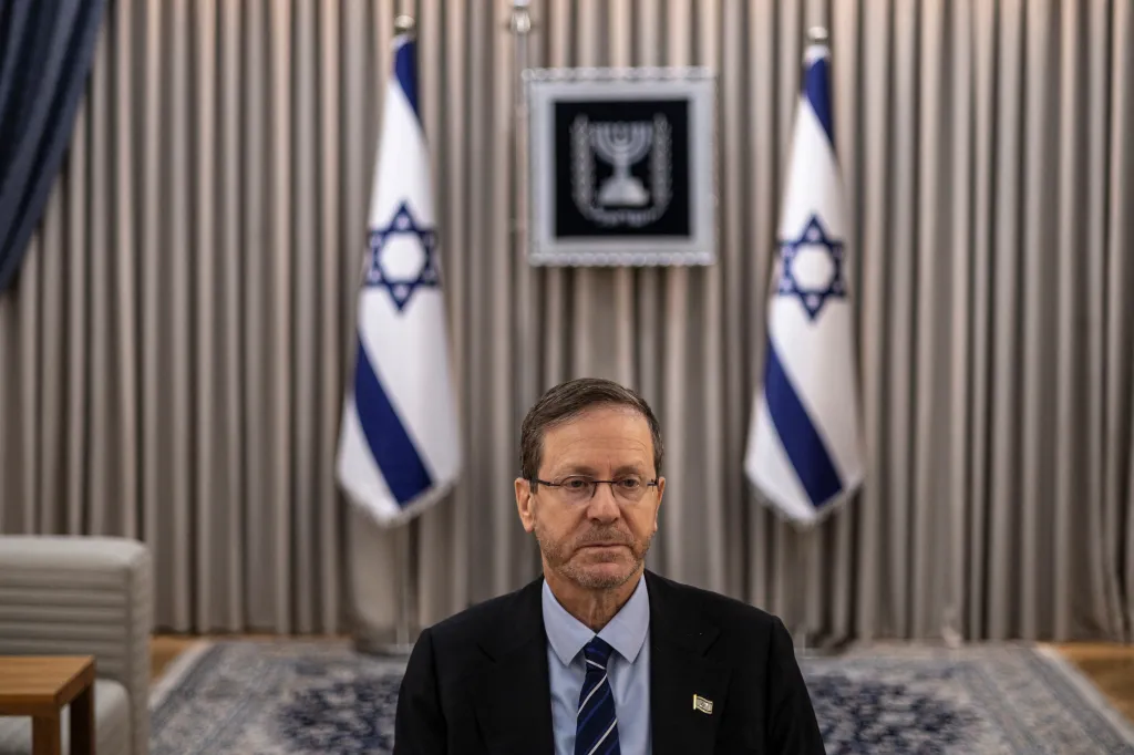 Isaac Herzog in a suit and tie, with Israeli flags and the state emblem behind him.