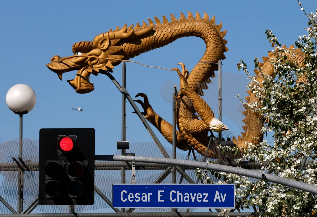 A street sign for Cesar E Chavez Av, a red traffic light, and a golden dragon sculpture against a blue sky.