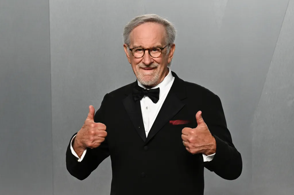 Steven Spielberg smiling and giving two thumbs up while wearing a tuxedo.