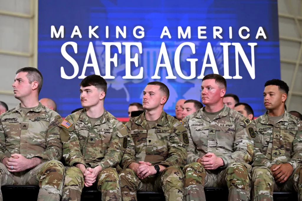 Five U.S. Army National Guard members in camouflage uniforms sit looking forward, with a blue background behind them reading 