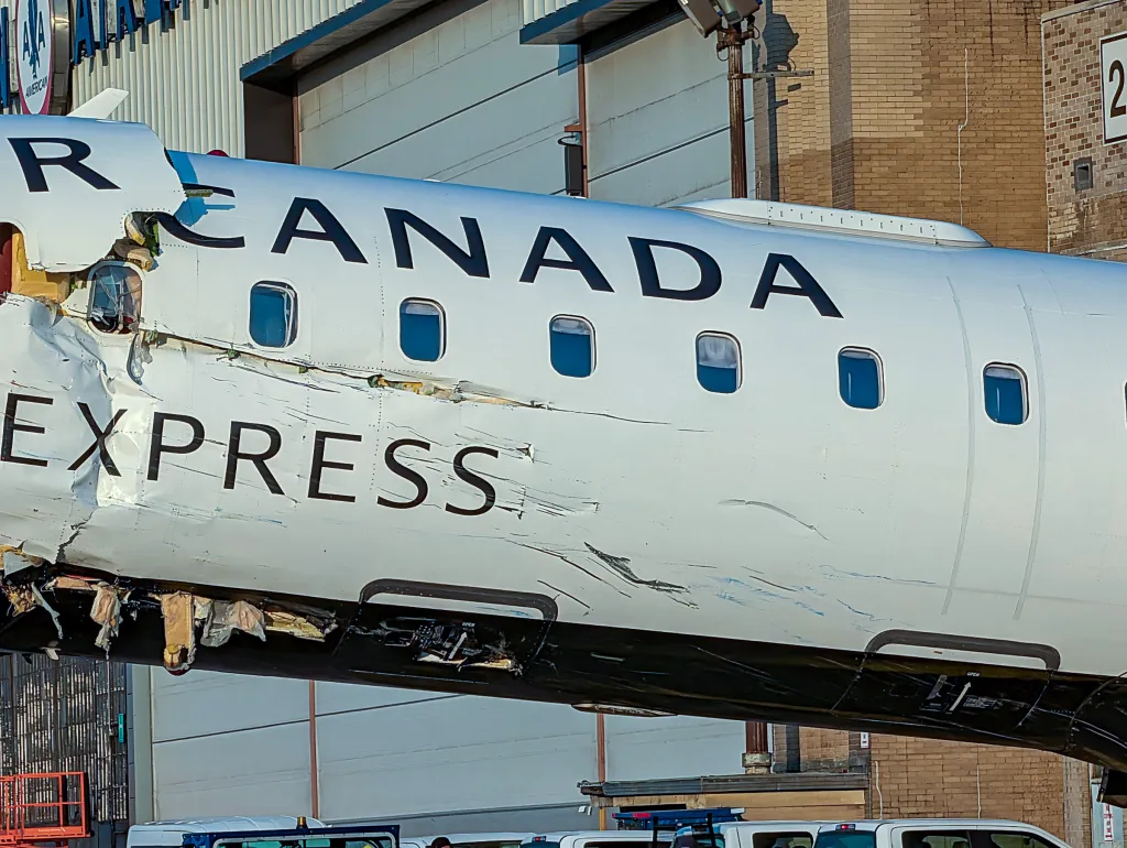 Damaged Air Canada Express plane with a large tear and scratches on its fuselage.