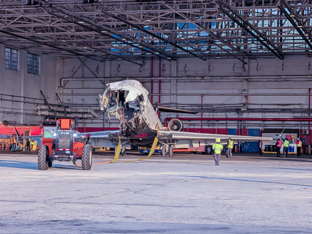 Air Canada plane with extensive damage to its nose and fuselage is moved into a hangar to unload passengers' personal belongings.