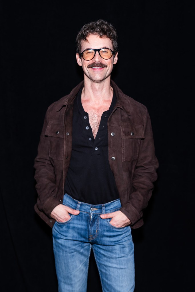 Brad Goreski poses for a photo in a brown suede jacket and blue jeans.