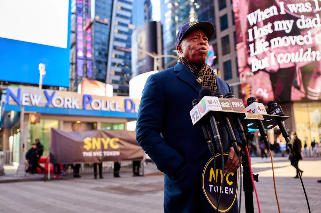 Former NYC Mayor Eric Adams speaking at a press conference in Times Square, holding an 