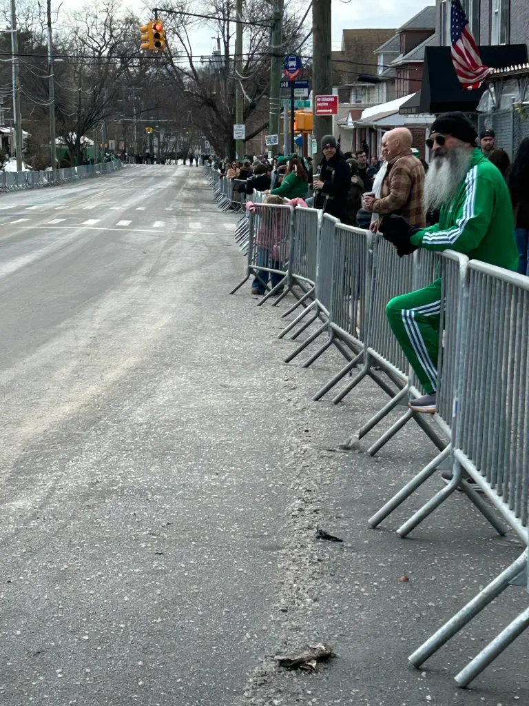 Spectators in green attire waiting behind barriers at the Staten Island St. Patrick's Day parade.