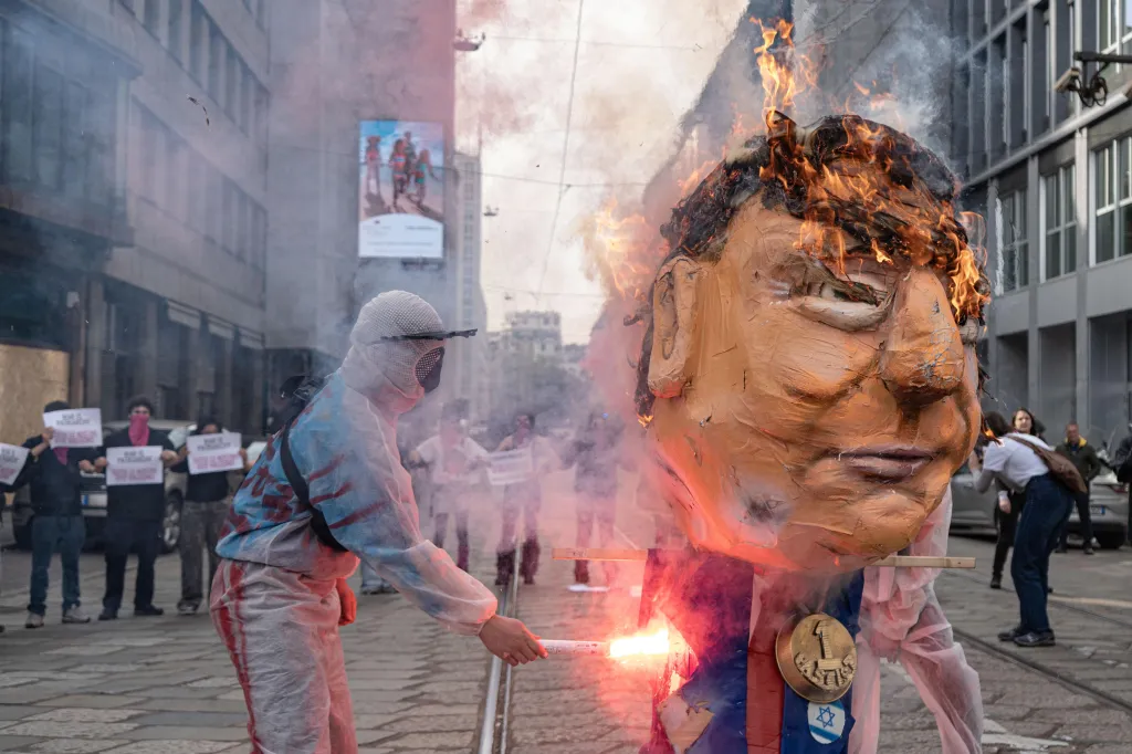 A person in a protective suit and mask sets an effigy of Donald Trump ablaze during a transfeminist student strike in Milan, Italy.