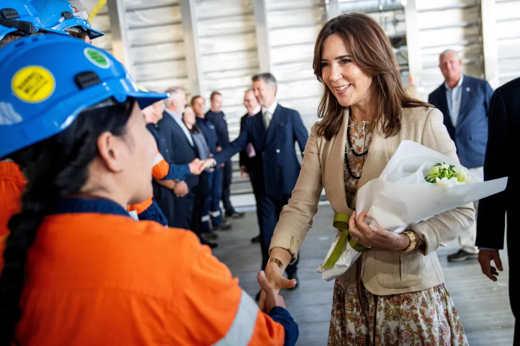 Queen Mary shaking hands with a person in a blue hard hat and orange shirt.