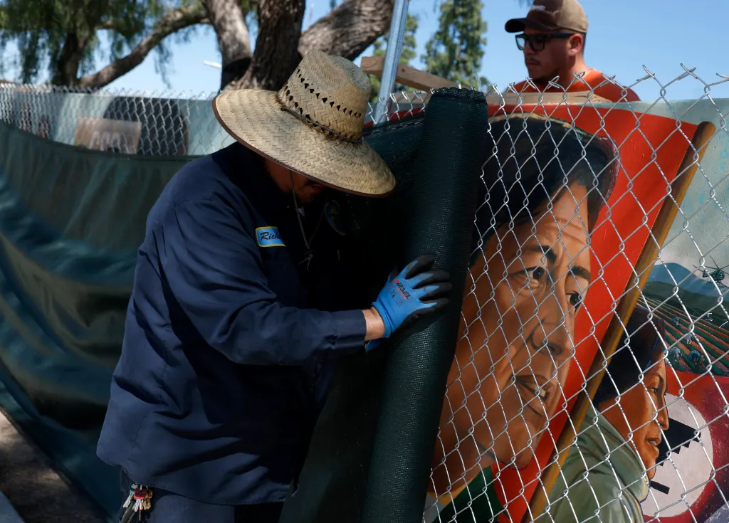 City workers covering a mural of Cesar Chavez with a dark screen.