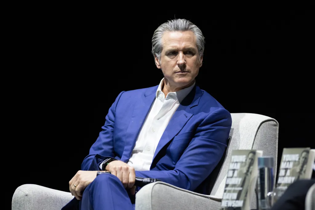 California Governor Gavin Newsom sits in a chair at an event promoting his book, 