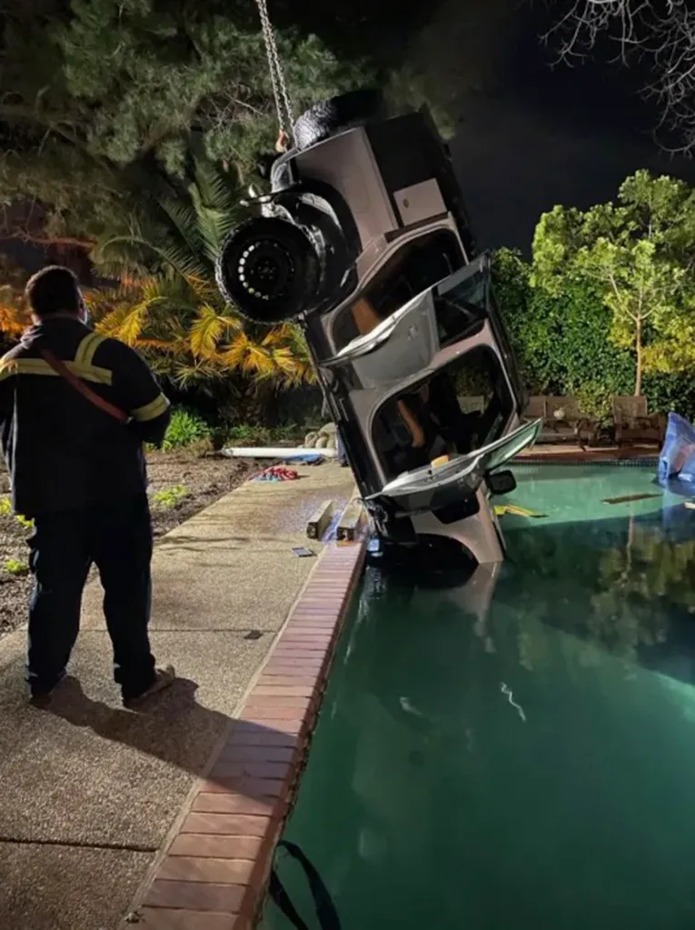 A Land Rover Defender being pulled by a crane out of a swimming pool at night.