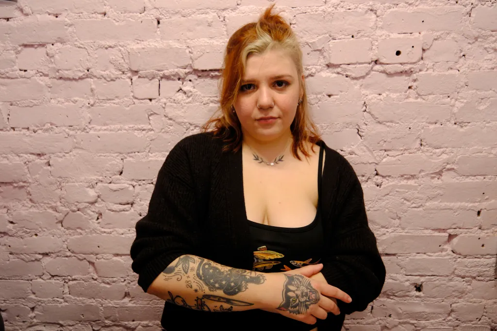Samantha Vargas, a piercing artist, stands against a white brick wall.