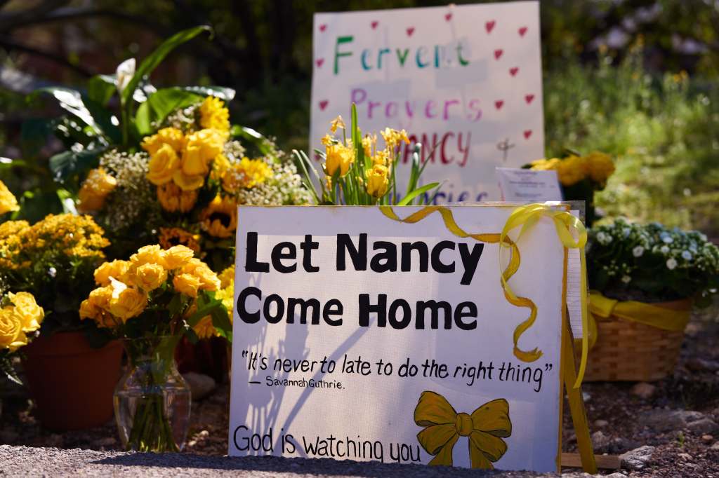 A makeshift memorial with signs and yellow flowers reading