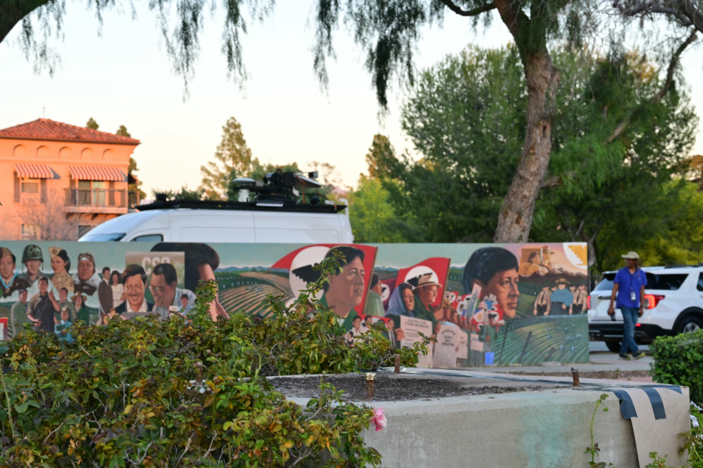 A low-angle photo showing a mural of Cesar Chavez and farmworkers, with a concrete pedestal in the foreground where a statue was removed.