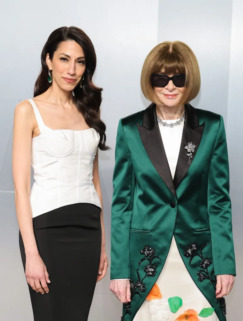 Huma Abedin , in a white corset top and black skirt, and Anna Wintour, in a green tuxedo jacket and white gown and sunglasses, stand together at the Vanity Fair Oscar Party.