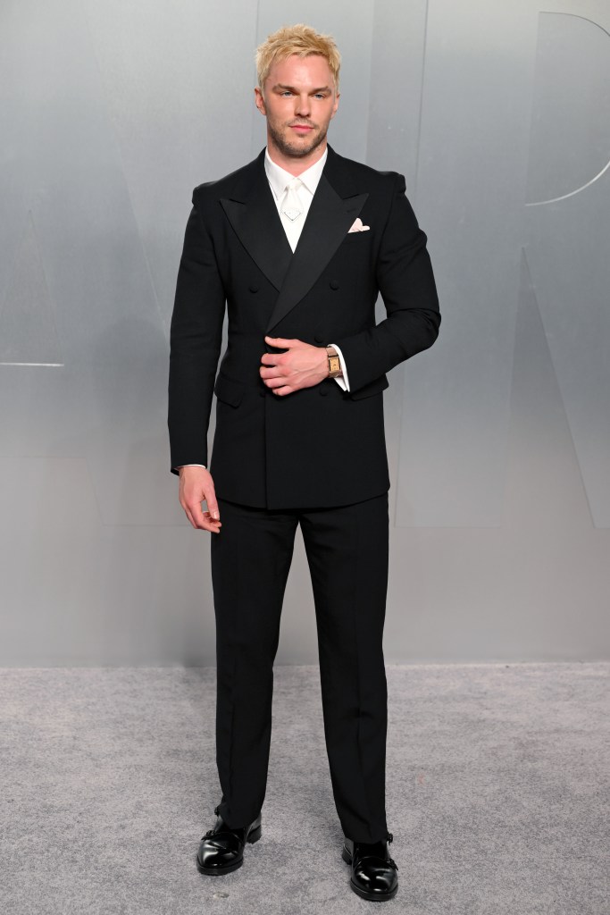 Nicholas Hoult wearing a black double-breasted tuxedo with a white tie and a gold watch.