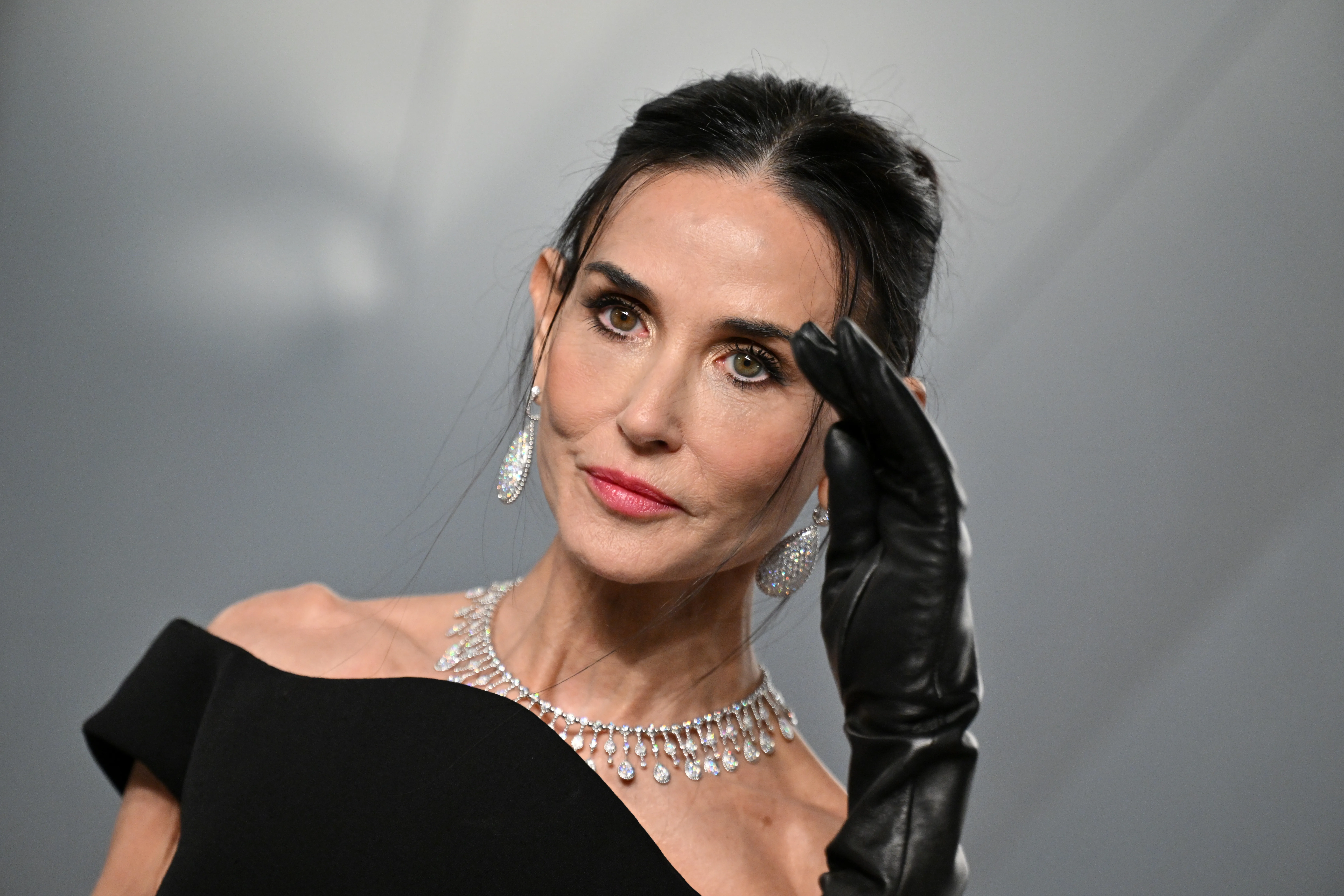 Demi Moore wearing an off-the-shoulder black gown, diamond necklace and earrings, and a black leather glove at the 2026 Vanity Fair Oscar Party.
