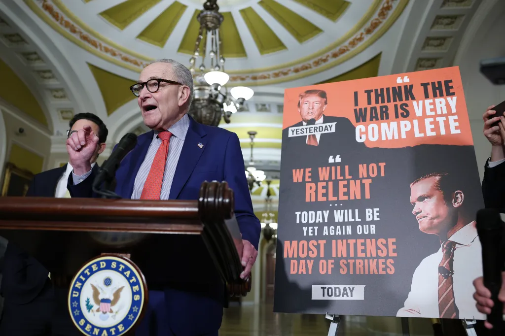 U.S. Senate Minority Leader Chuck Schumer speaking at a news conference with a protest sign referencing statements from Donald Trump and J.D. Vance.