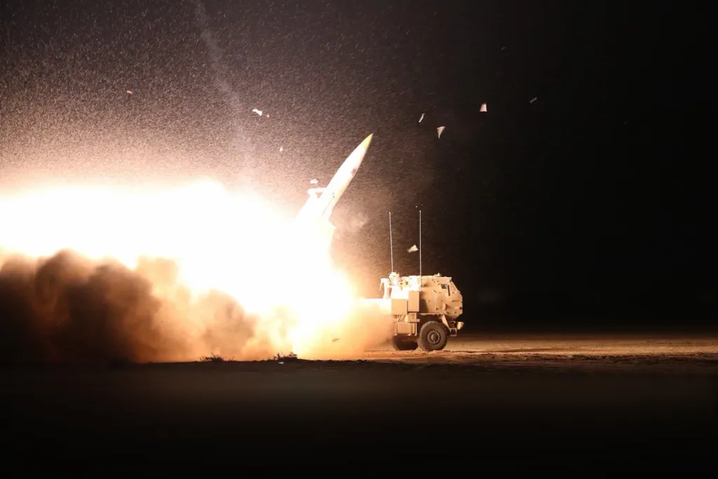 A large missile launches from a vehicle at night, surrounded by bright light and smoke.
