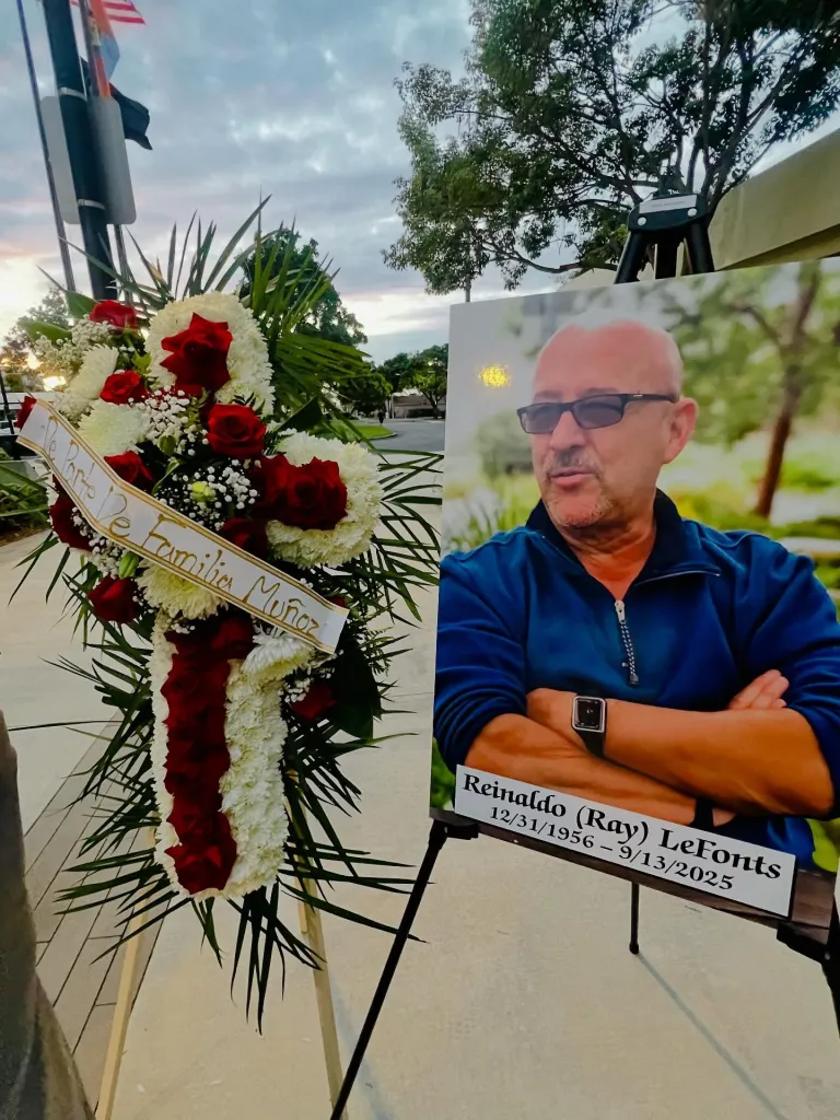 A memorial photo of Reinaldo (Ray) LeFont and a floral cross arrangement that says 