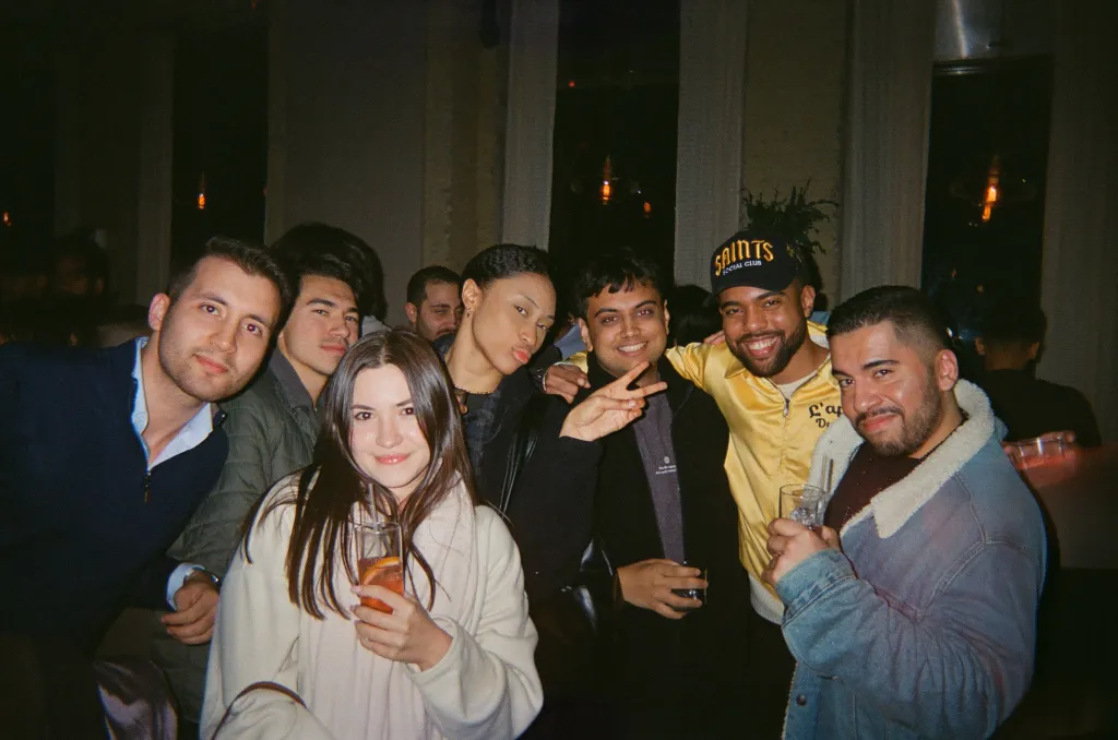 A diverse group of young adults smiling for the camera at a social gathering.