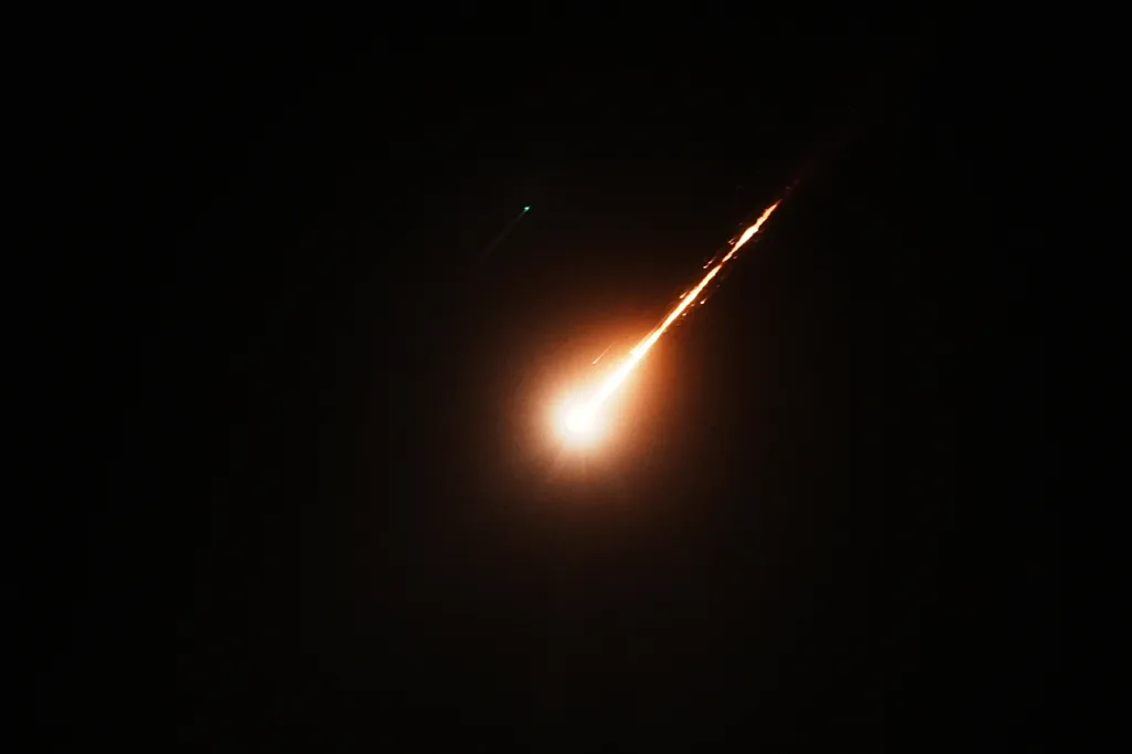 A bright, fiery streak of light resembling a missile shoots diagonally across a dark night sky.