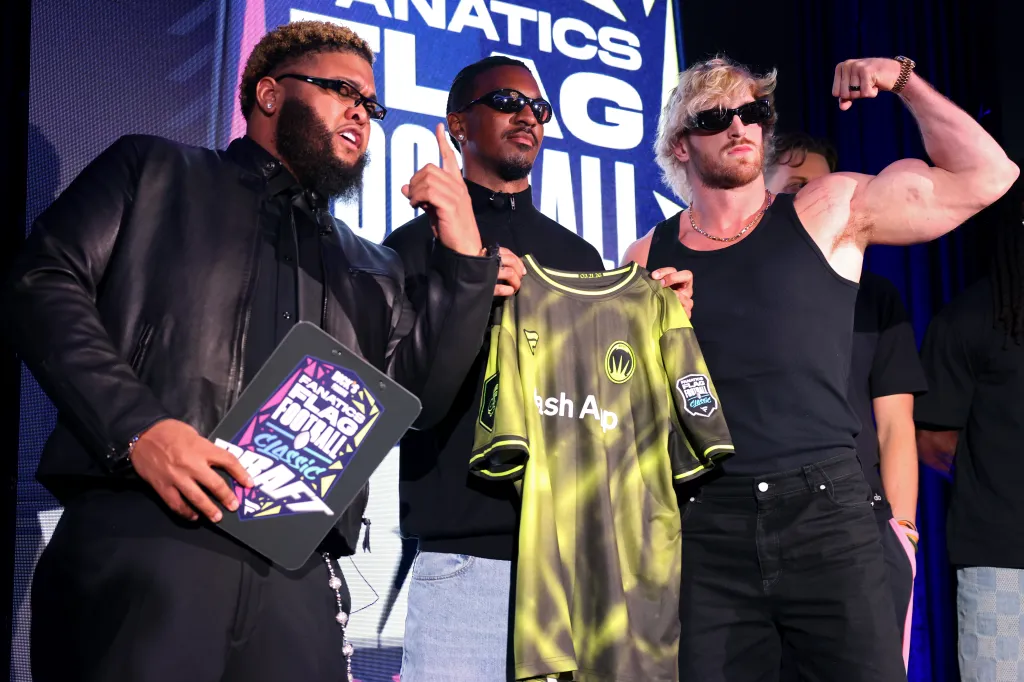 Three men at the Fanatics Flag Football Classic Draft event: one holds a clipboard, one holds a jersey, and one flexes his arm.