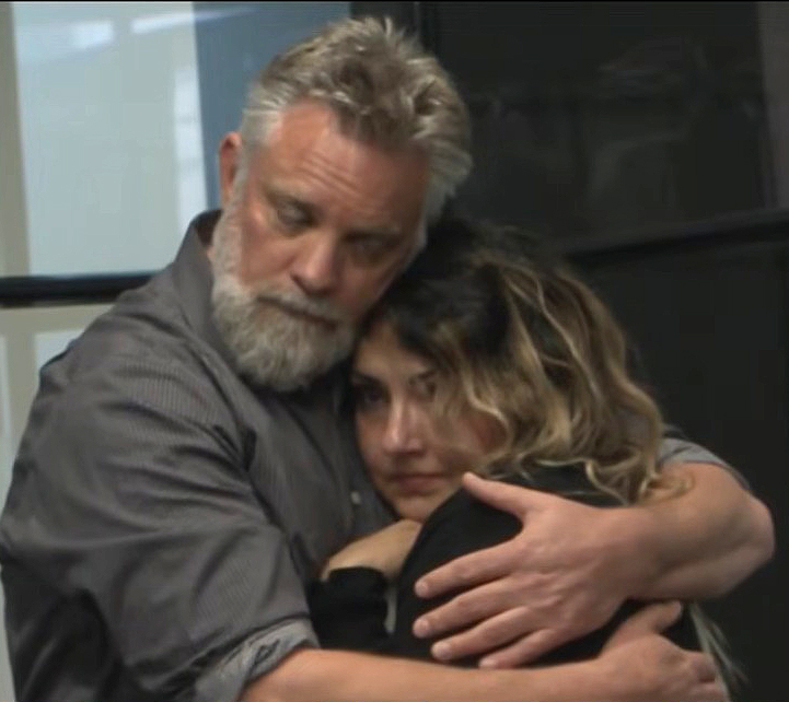 A man with a gray beard embraces a woman with curly brown hair.