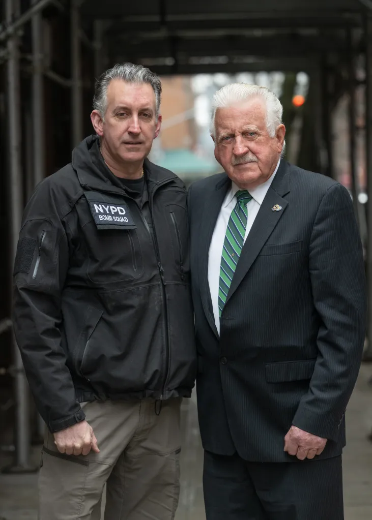 Detective Denis Mulcahy and his son Detective Sean Mulcahy, both dressed in professional attire, pose for a photo.