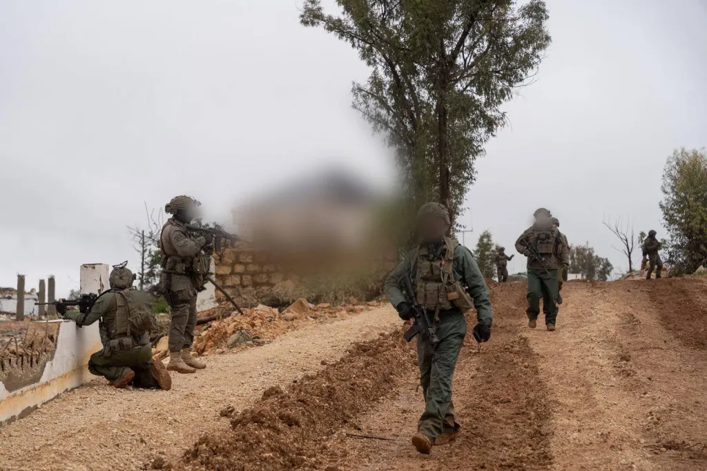 Israeli soldiers from the 91st Division conduct targeted ground operations in Southern Lebanon, with one soldier walking forward, another kneeling, and others in the background amidst debris and a muddy track.