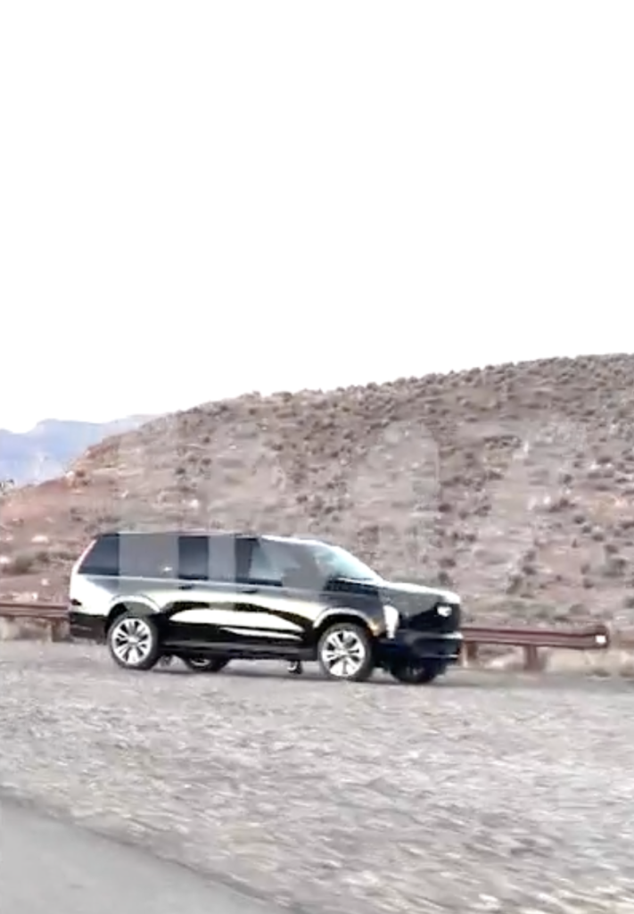 A black SUV driving past a dry, rocky hillside.