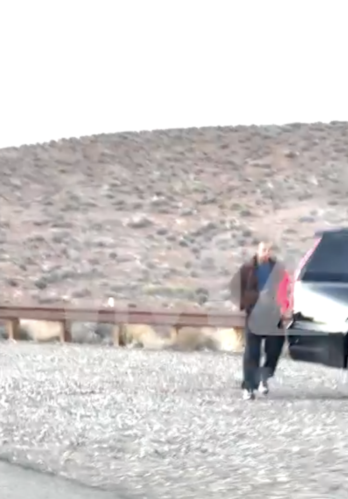 A person walking on a road next to a large hill.