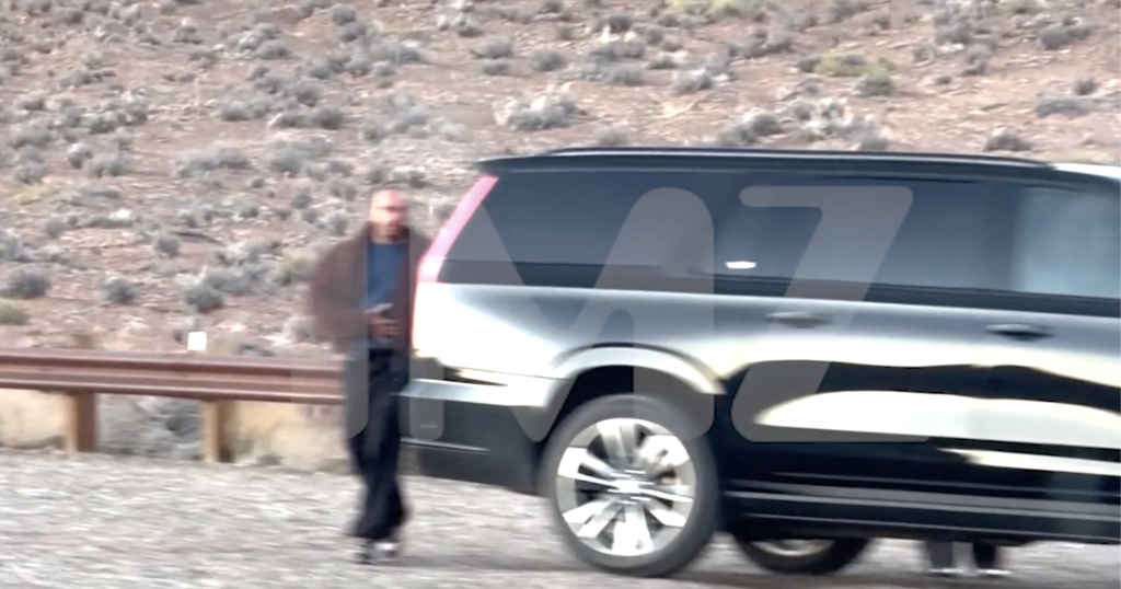 Lewis Hamilton walking next to a black SUV in a desert landscape.