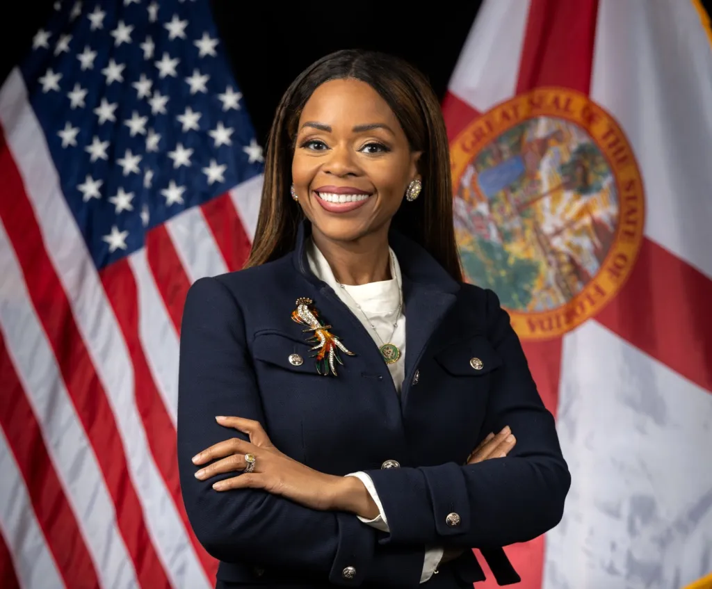 Congresswoman Sheila Cherfilus-McCormick smiling with US and Florida flags in the background.