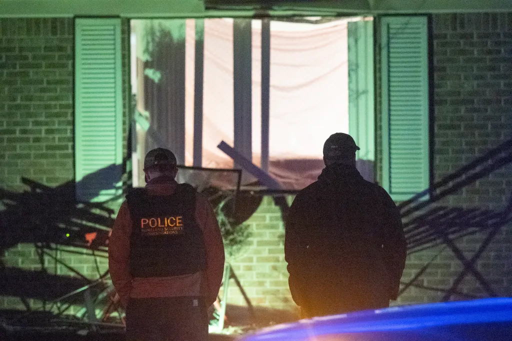Two police officers standing in front of a damaged house at night.